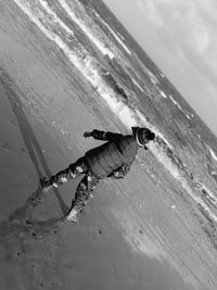 Tilt image of boy wearing warm clothing while standing on shore at beach