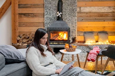 Woman using laptop while sitting by fireplace at home
