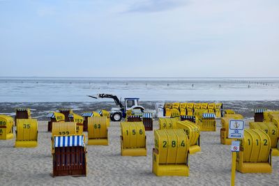 Hooded chairs on beach against sky