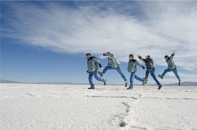 Multiple image of man jumping on salt flat against sky