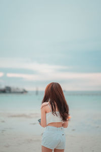 Rear view of woman standing at beach against sky