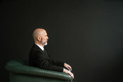 Side view of man sitting against black background