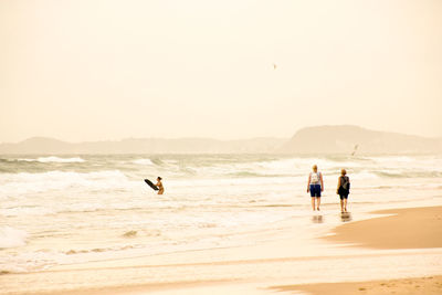 Rear view of female friends walking on shore at beach