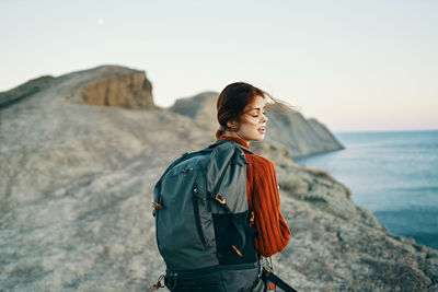 Young woman standing on rock by sea against sky