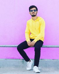 Young man wearing sunglasses standing against wall