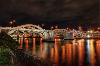 Illuminated bridge over river against sky at night