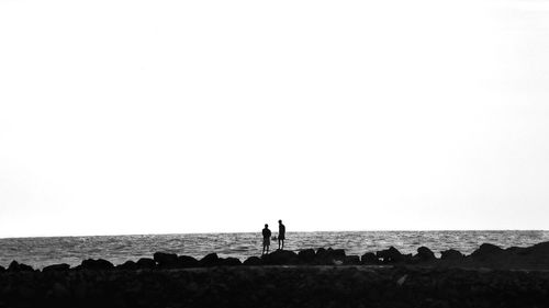 People standing on rocks by sea against clear sky