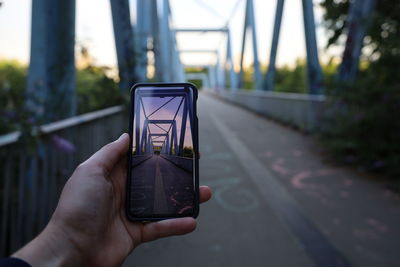 Hand of person using mobile phone to take picture of a bridge 