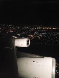 Airplane flying over illuminated city against sky at night