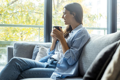 Young woman using phone while sitting on sofa at home