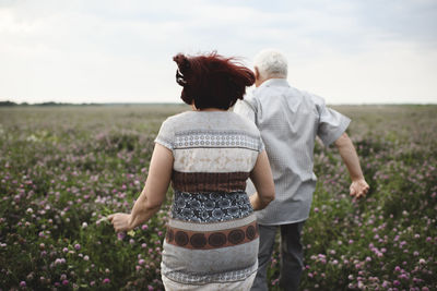Back view of senior couple running on flower meadow