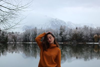 Woman with hand in hair standing by lake during winter