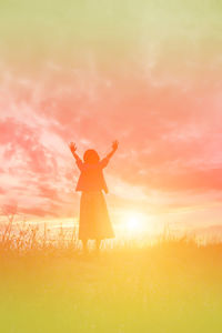 Woman standing on field against orange sky