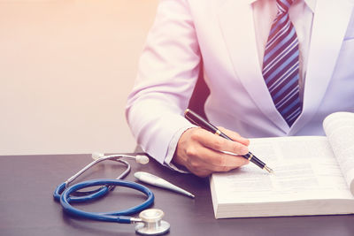 Midsection of doctor writing prescription on book at table