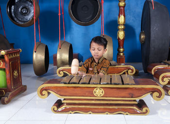 Smiling boy holding hammer sitting by musical instrument