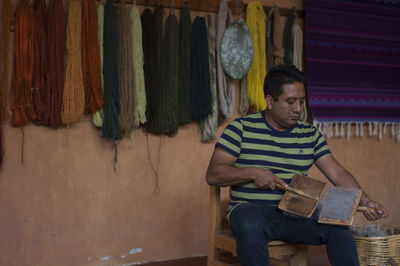 Young man looking away while sitting on wood against wall