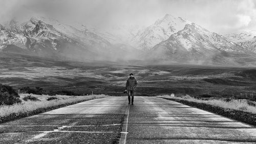 Full length of man walking on walkway against snowcapped mountains