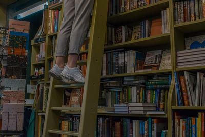 Low section of person standing on ladder by bookshelf