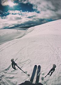 Low section of person skiing on snowcapped mountain against cloudy sky