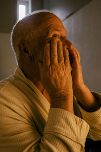 Elderly man applying moisturizer on face in bathroom