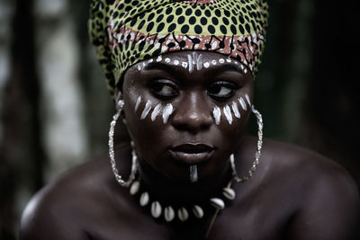 African woman sitting in the aburi forest in ghana with white painting on her face and headdress
