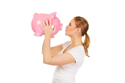 Side view of young woman puckering at piggy bank against white background