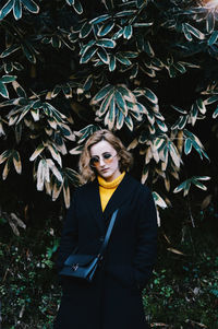 Portrait of beautiful woman in sunglasses standing against tree