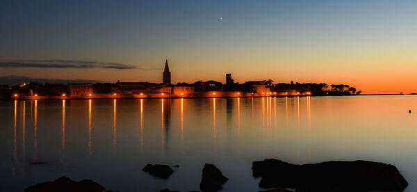 Silhouette buildings by sea against sky during sunset