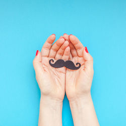 Cropped hands of woman holding party prop against blue background