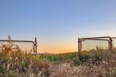 Fence on field against clear sky during sunset