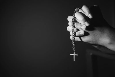 Image black and white woman hand holding rosary against cross and praying to god at church.