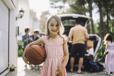 Portrait of smiling girl holding basketball with family in background