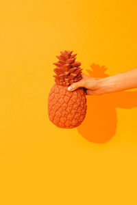 Hand holding creative pineapple on yellow background. minimal. stylish still life.