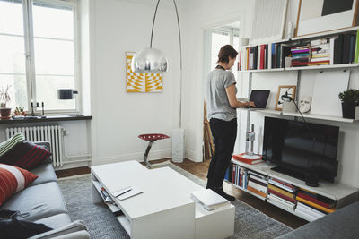 Rear view of industrial designer using laptop at shelf in home