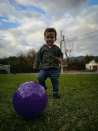 Portrait of cute baby boy playing with ball standing on grassy field