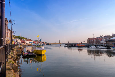 Sailboats moored on river by buildings in city against sky