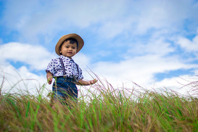 Portrait of cute boy standing on grassy field against sky