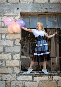 Happy woman having fun holding colorful air balloons on a broken window