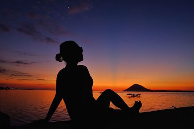 Silhouette woman sitting on beach against sky during sunset