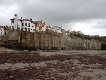 Low angle view of buildings by beach against cloudy sky