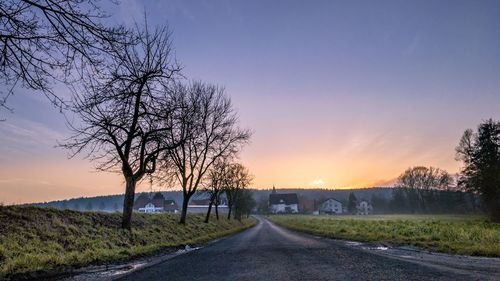 Road amidst bare trees against sky during sunset