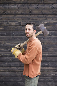 Portrait of man holding axe while standing against cabin