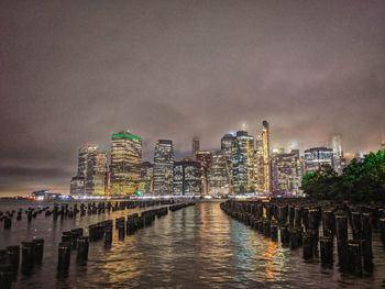 Illuminated buildings by river against sky in city