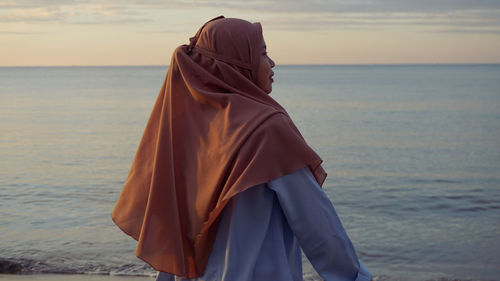Midsection of woman at beach against sky during sunset