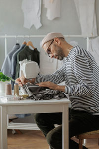 Senior male fashion designer or clothing constructor sews on a sewing machine in the workshop 