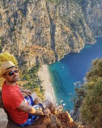 High angle view of man sitting at cliff against sea