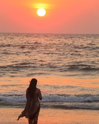 Silhouette woman standing at beach against sky during sunset