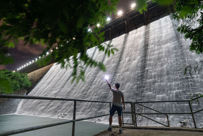 Rear view of man standing by railing against waterfall