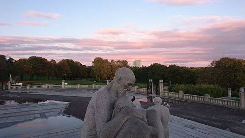 Man and woman on retaining wall against sky during sunset