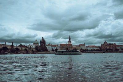 View of buildings by river against cloudy sky